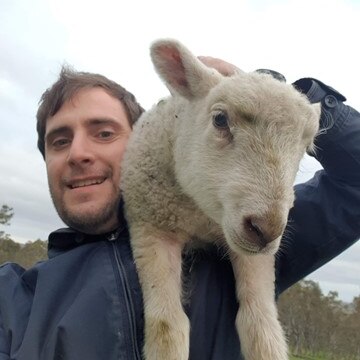 a happy man holding a baby lamb on his shoulder.