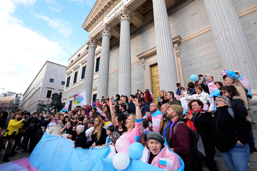 People holding pink blue and white balloons cheering
