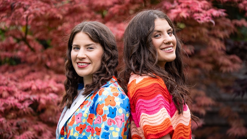 Twin sisters standing back to back smiling at the camera in very colourful tops