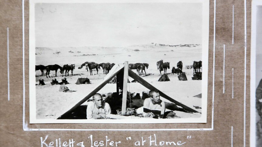 Black and white photo of two men lying under an open tent in the desert.