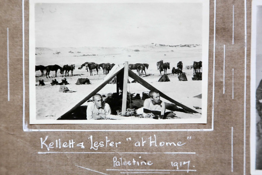 Black and white photo of two men lying under an open tent in the desert.