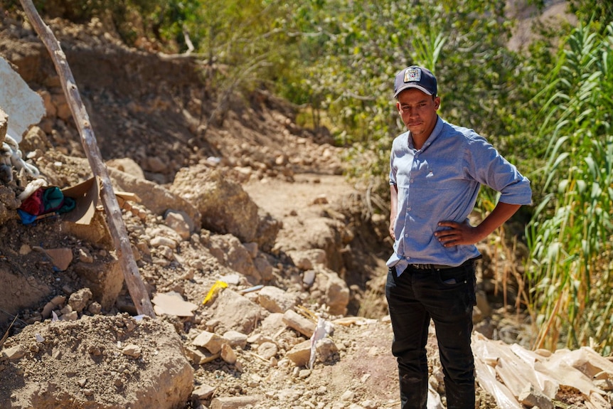 A man with his hands on his hips next to a pile of rubble, looking on 