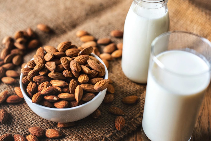 A bowl of almonds next to a glass and bottle of milk on a hessian surface.