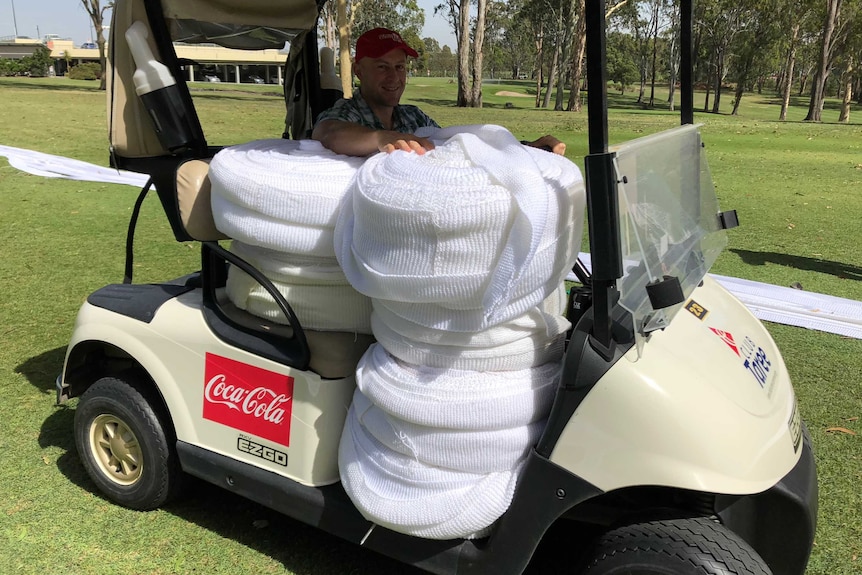 A man in a golf buggy with big round bales of white knitting.