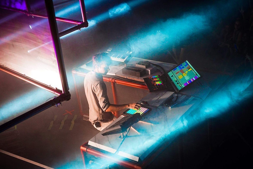 Sydney musician Flume stands at a table playing electronic instruments during a concert