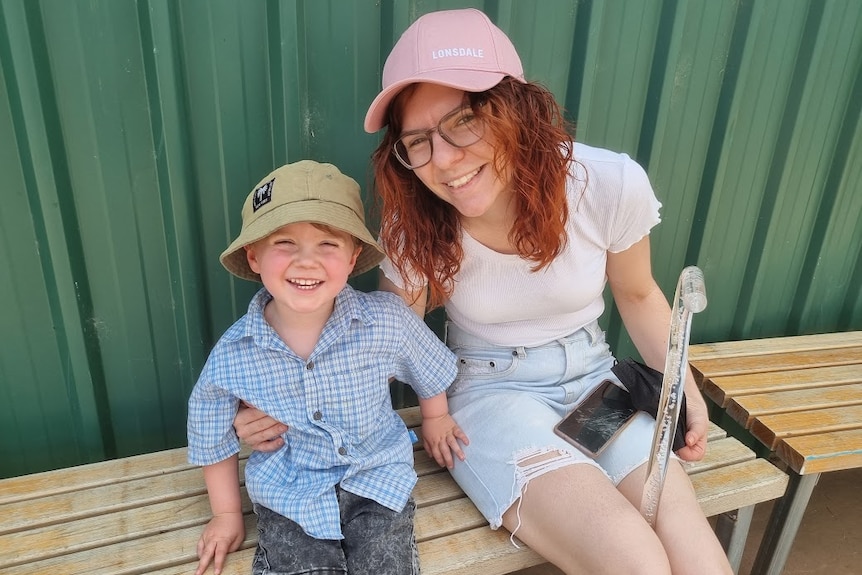 A woman and a boy, both sitting on a bench, smile up at the camera.