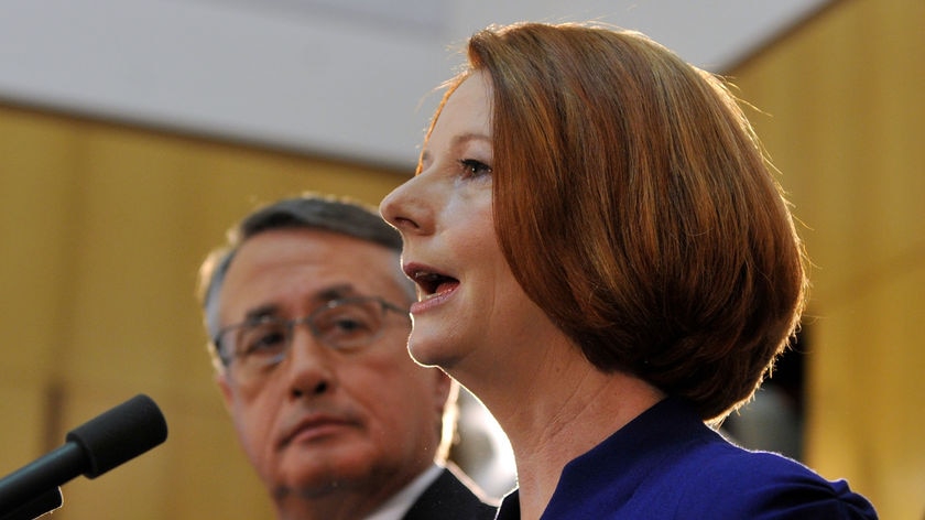 Federal Treasurer Wayne Swan listens to Prime Minister Julia Gillard's carbon tax announcement