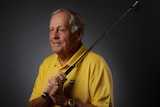 An elderly man wearing a yellow shirt carries a golf club over his left shoulder