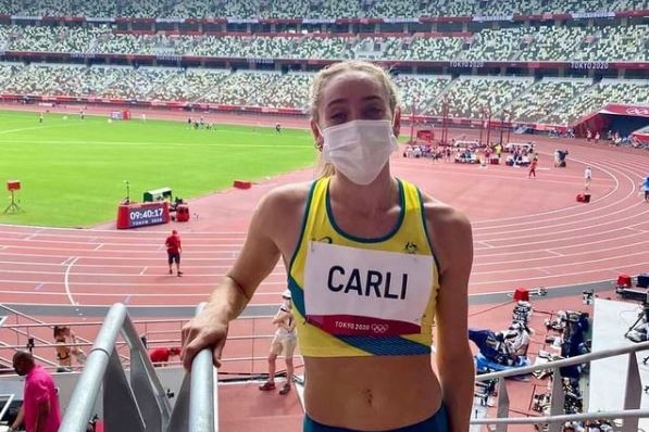 Srah Carli stands in her running gear inside the Tokyo Olympics stadium wearing a white mask.