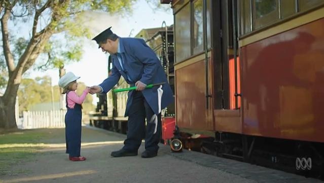 A train conductor shakes hands with a young child beside an old train