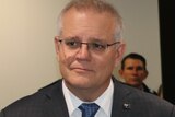 A mid-shot of a smiling Prime Minister Scott Morrison indoors wearing a suit and tie.