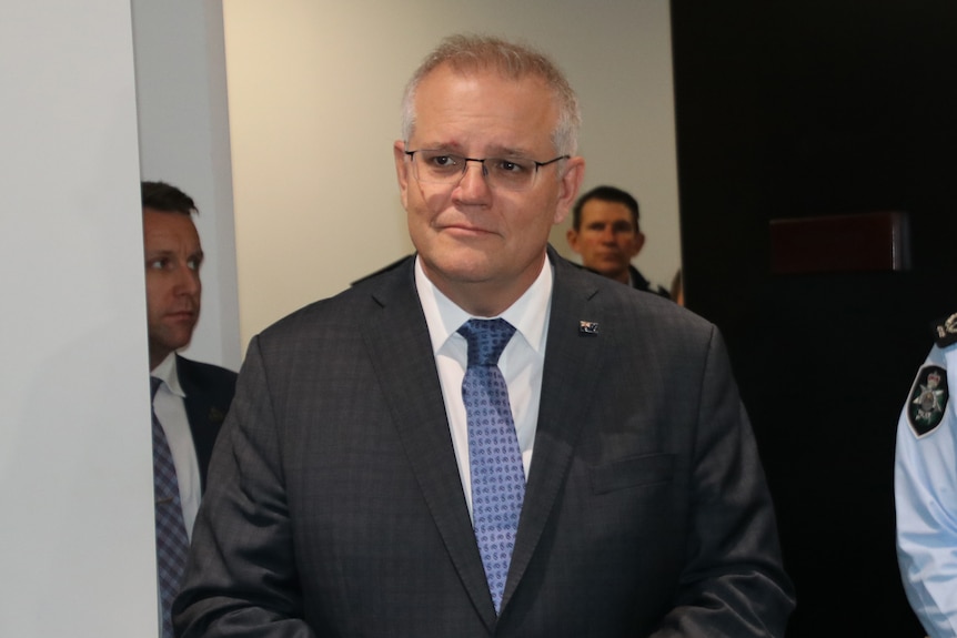 A mid-shot of a smiling Prime Minister Scott Morrison indoors wearing a suit and tie.
