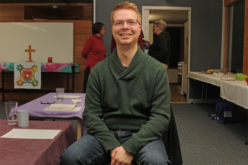 Young man with blonde hair and glasses smiling inside a Neighbourhood Centre.
