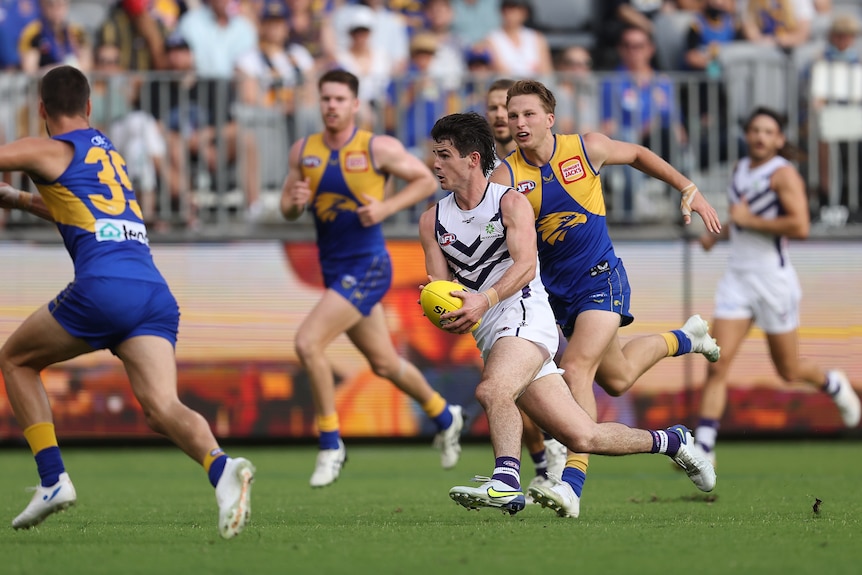 An AFL footballer looks to change direction as he runs with the ball through the opposition defence during a game.