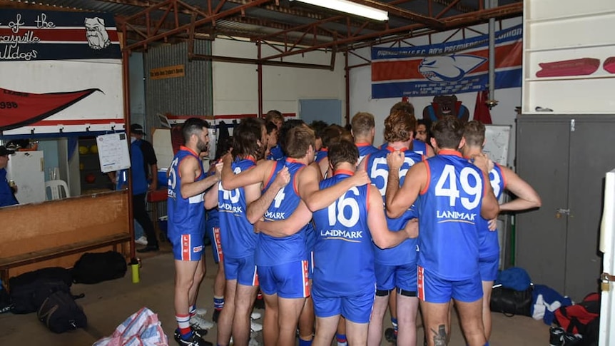A group of men wearing red, blue and white football jumpers stand in a huddle. 