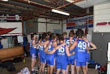 A group of men wearing red, blue and white football jumpers stand in a huddle. 