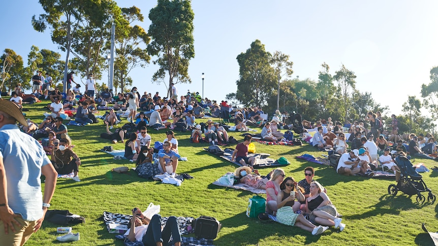 Scores of people lie on blankets and the grass on a hill in Barangaroo.