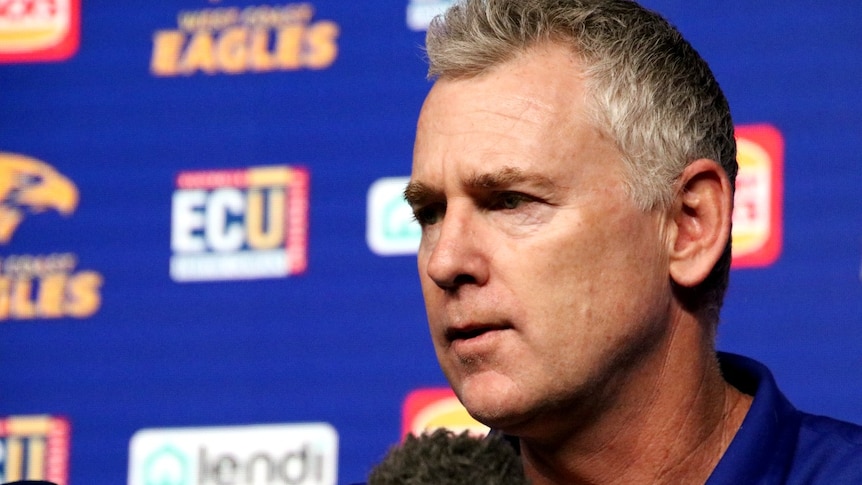 A close-up photo of Adam Simpson in front of a West Coast Eagles banner at a press conference.