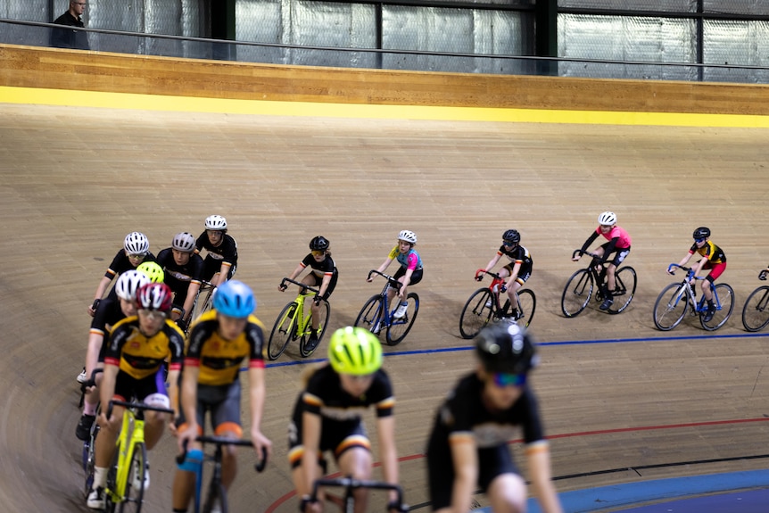 Young boys and girls cycling in a uniform line around a velodrome.