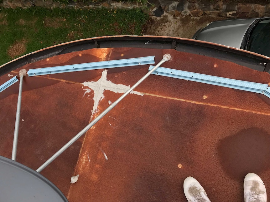 Two shoes visible on rusty roof with metal strips attached to it haphazardly.