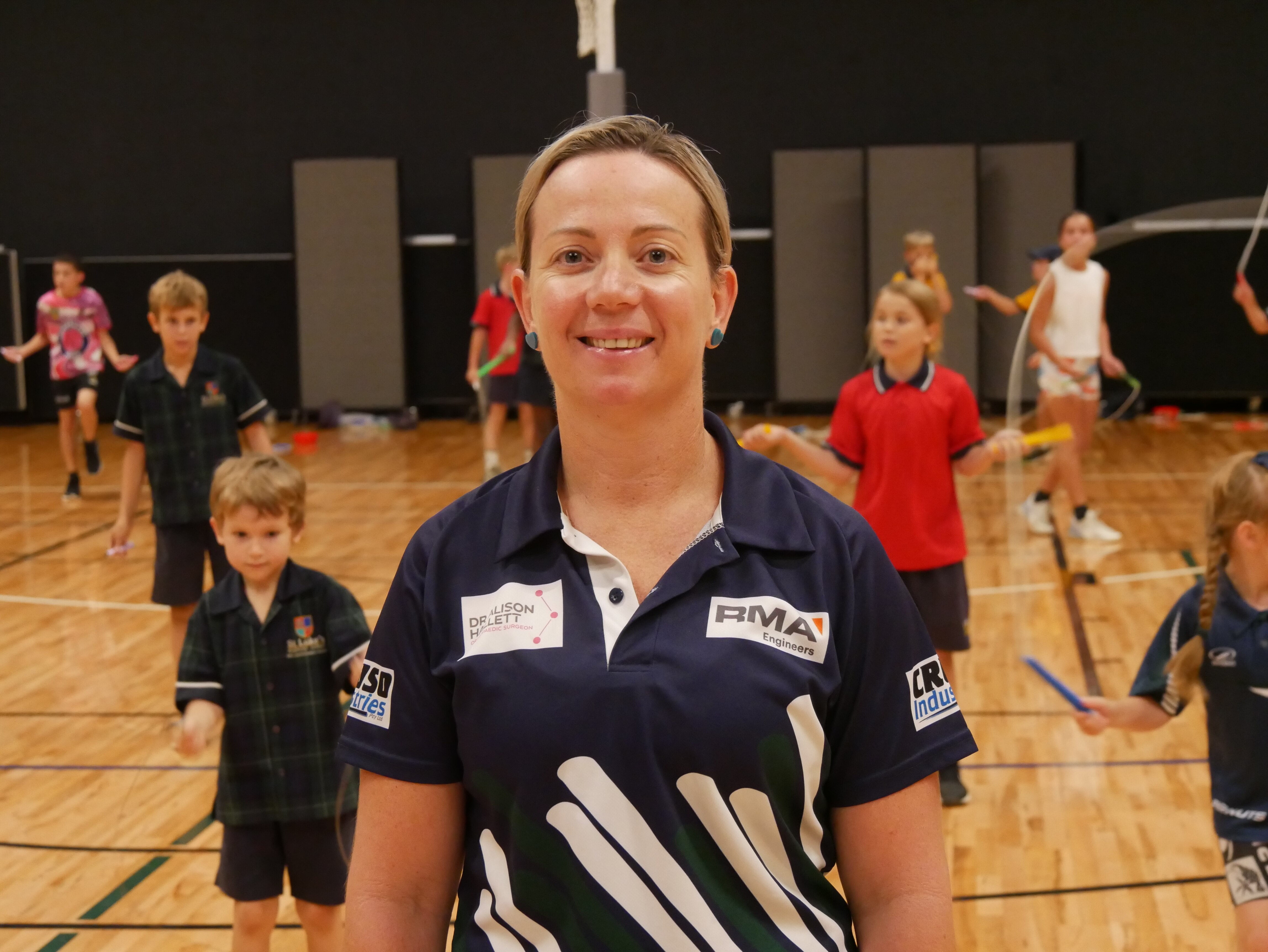 A woman smiling with school students skipping behind her