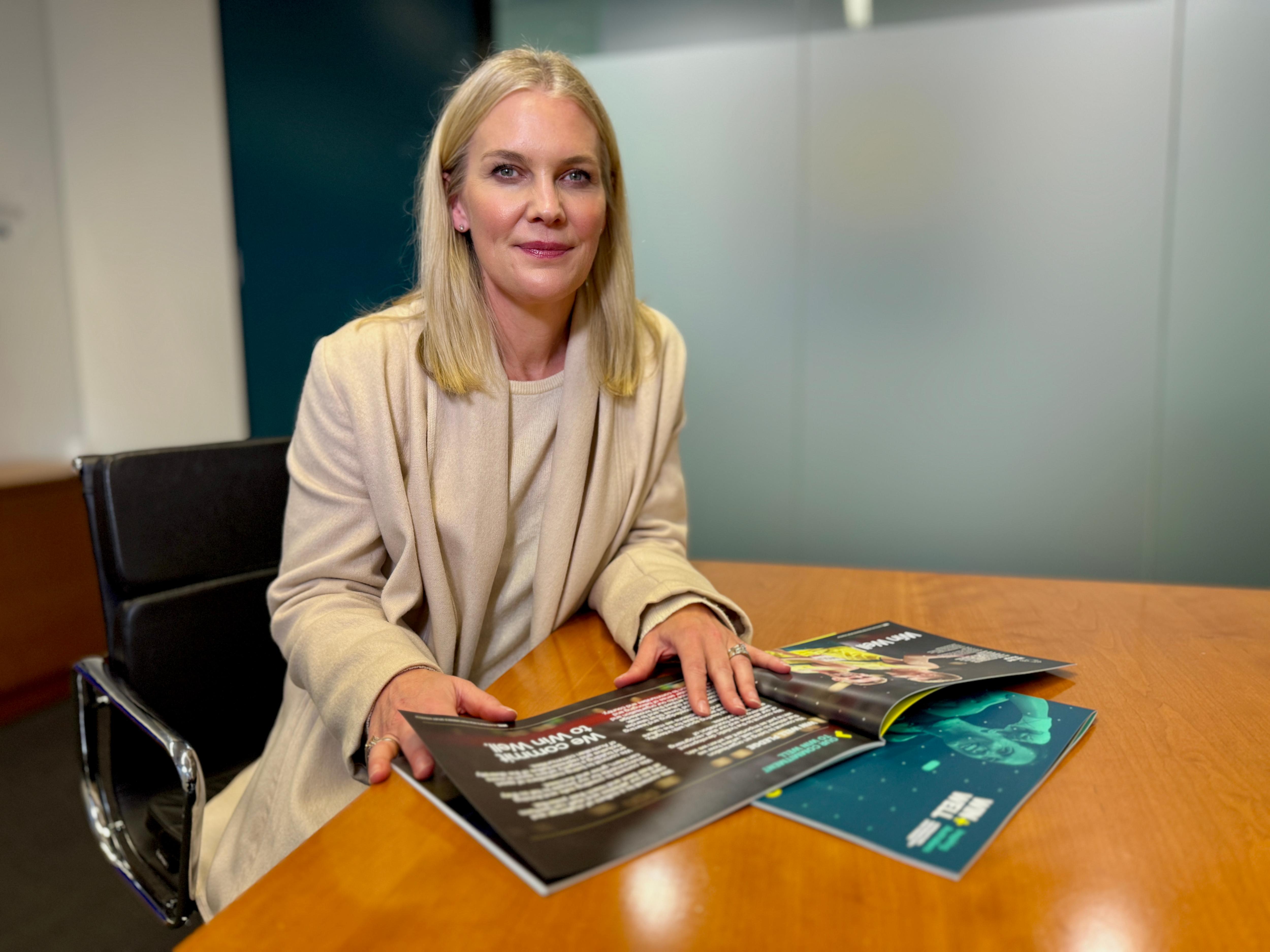 AIS Director Matti Clements, a white woman with shoulder length blonde hair, sits at an executive desk
