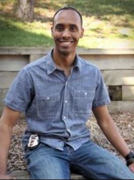 Minneapolis police officer Mohamed Noor sits on a wall outside in plain clothes smiling into the camera.