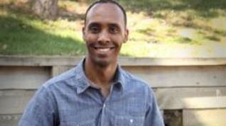 Minneapolis police officer Mohamed Noor sits on a wall outside in plain clothes smiling into the camera.