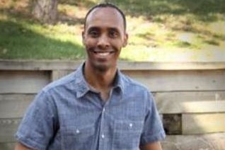 Minneapolis police officer Mohamed Noor sits on a wall outside in plain clothes smiling into the camera.