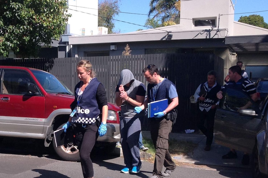 One of two men arrested (centre, with hood up) in the raid is led away by police.