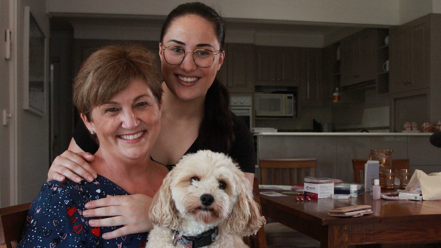 A mum and daughter cuddle at the kitchen table.