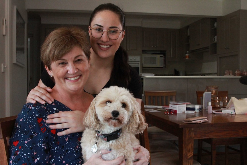 A mum and daughter cuddle at the kitchen table.