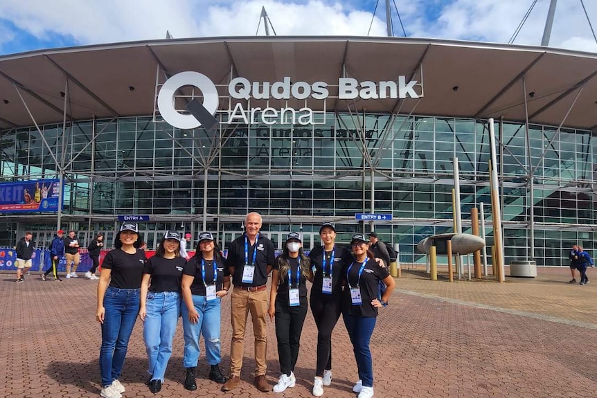 A group shot of seven people standing outside the Qudos Bank Arena.