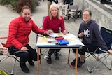 Three women sit at a fold out table with maps and highlighters and calculators on it