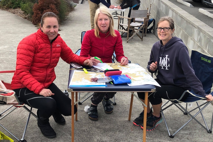 Three women sit at a fold out table with maps and highlighters and calculators on it