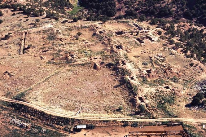 An aerial shot of desert. There are visible outlines of ruins and some greenery.