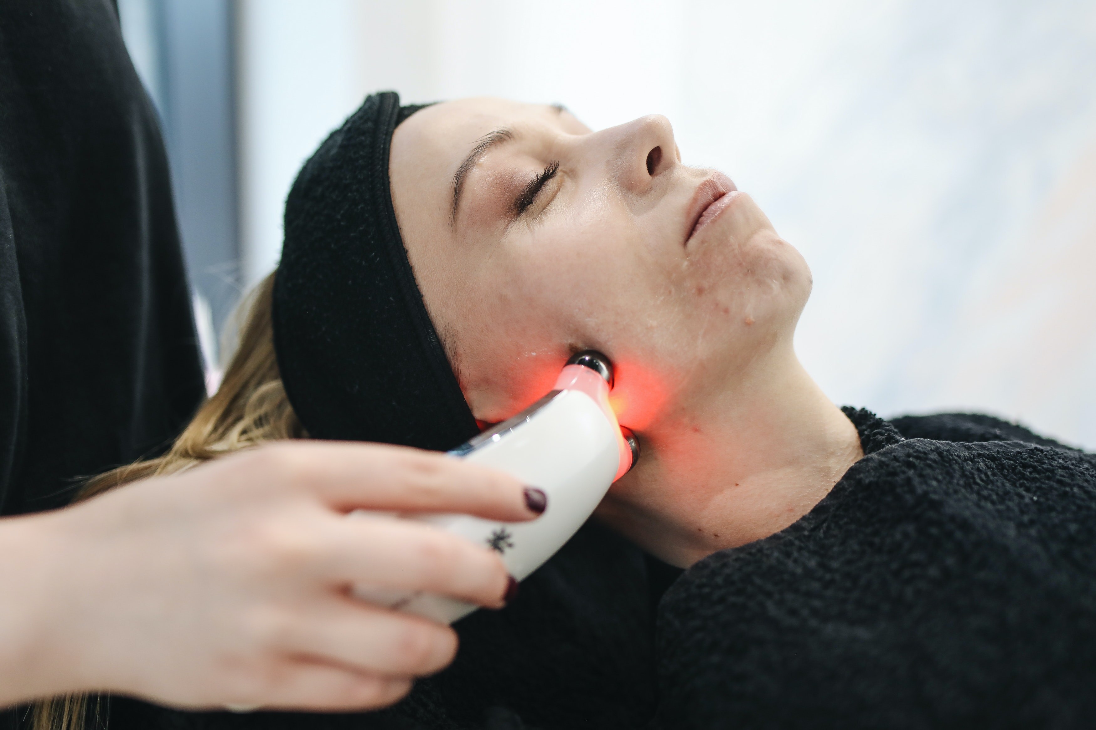 A woman lies on a salon bed as a laser tool is used on her face