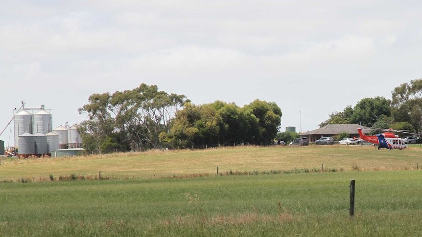 A helicopter sits in a paddock opposite a farm house.