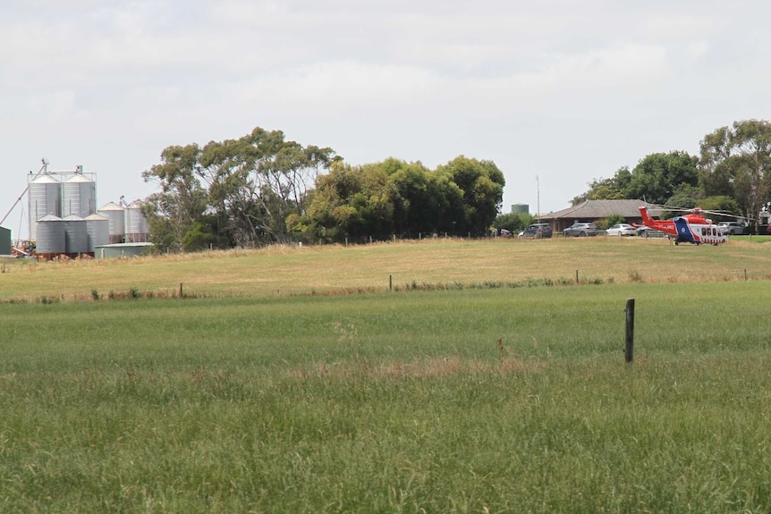 A helicopter sits in a paddock opposite a farm house.