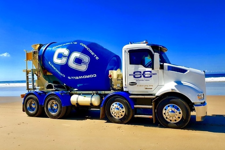 A cement mixing truck is on the beach with the ocean behind it