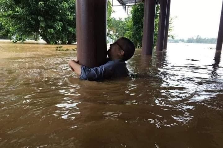 A man holding on to the bottom of a pier, while he's submerged in flood water.
