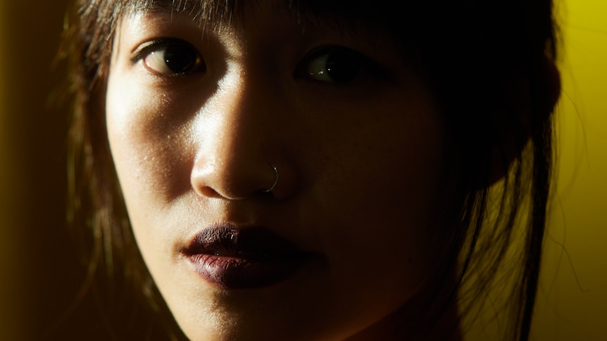 A photo of a young Asian woman with a fringe, one side of her face in shadow