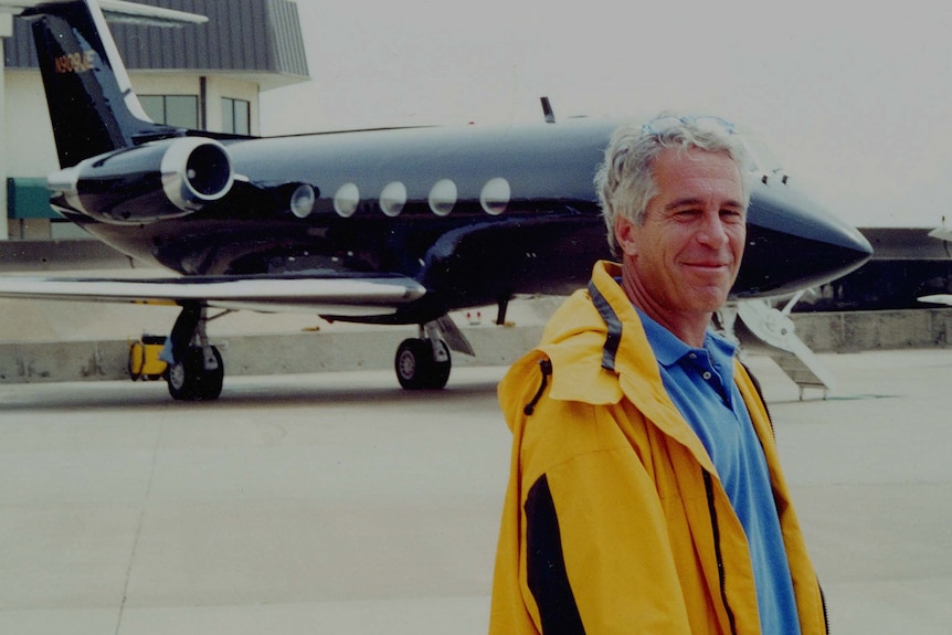 Jeffrey Epstein in a bright yellow jacket stands grinning in front of a small black plane 