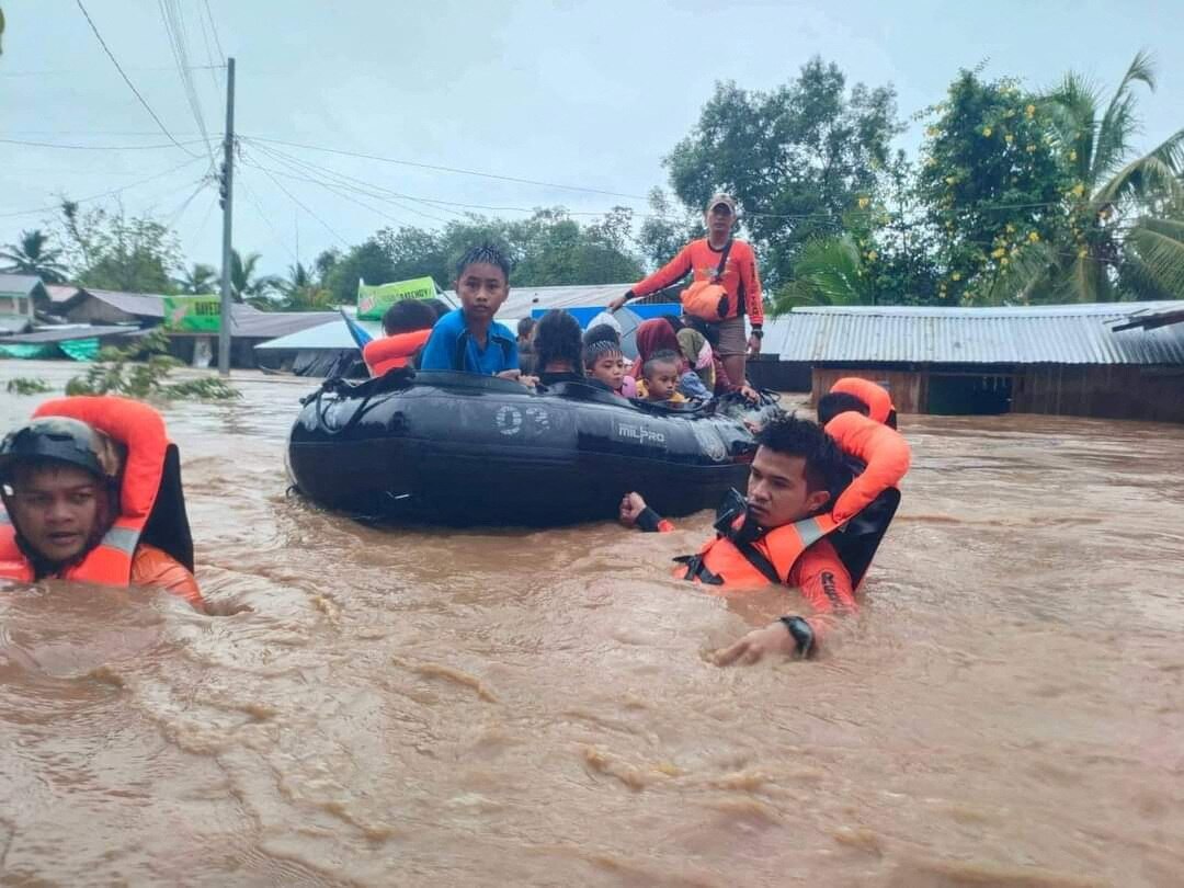 People in life jackets are rescued in a boat in a flooded river.