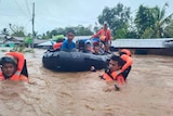 People in life jackets are rescued in a boat in a flooded river.