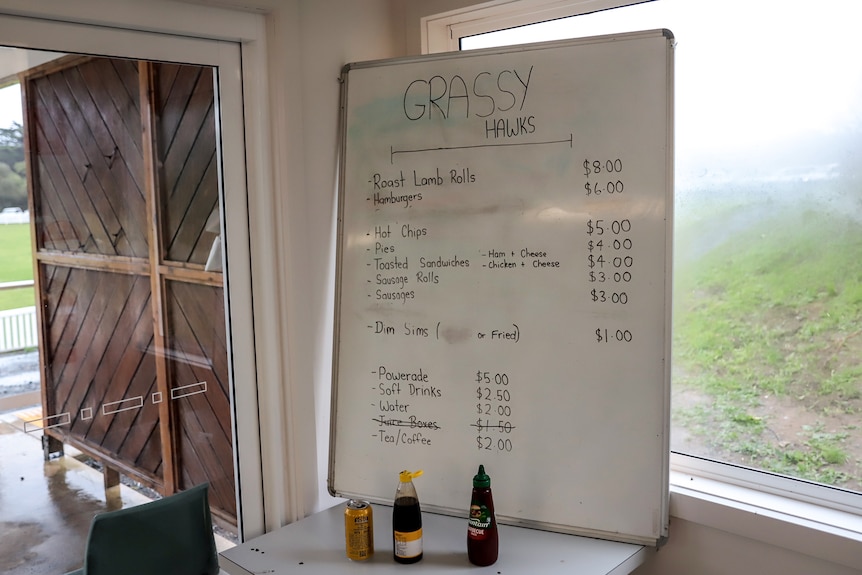 A whiteboard handwritten canteen menu rests against foggy window with football ground in background. 