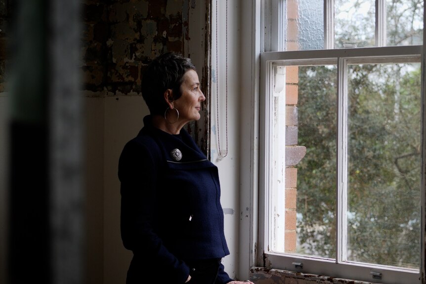 A woman standing near a window in a flood damaged room.