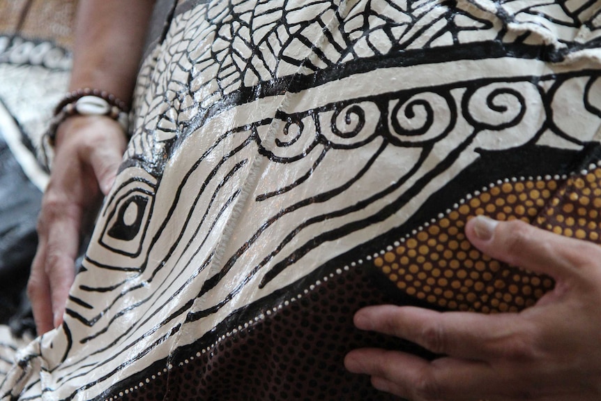 Two hands sit on either side of a whale's painted head, decorating a budbili, or possum-skin cloak.