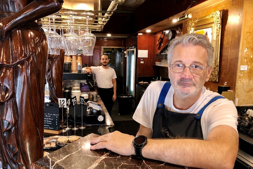 Roberto leans against the counter in an apron in his cafe.