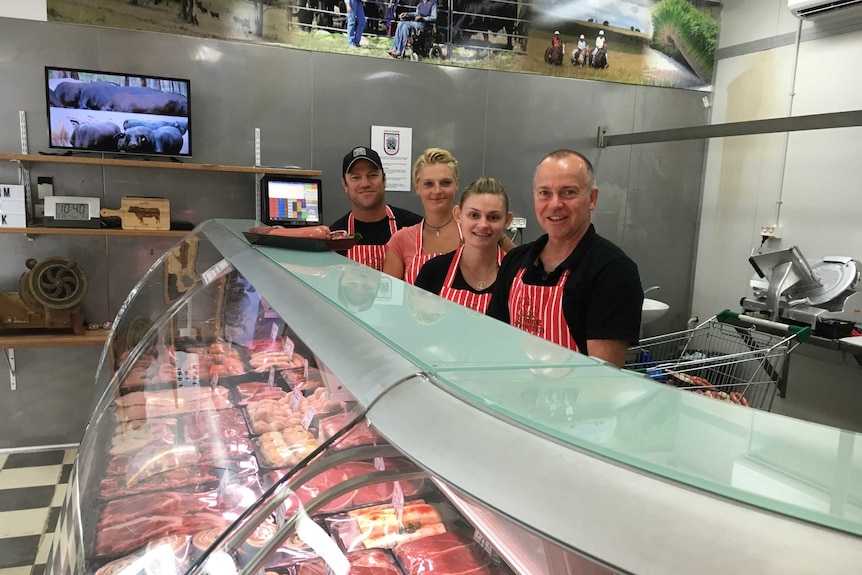 Four butchers stand behind the meat counter